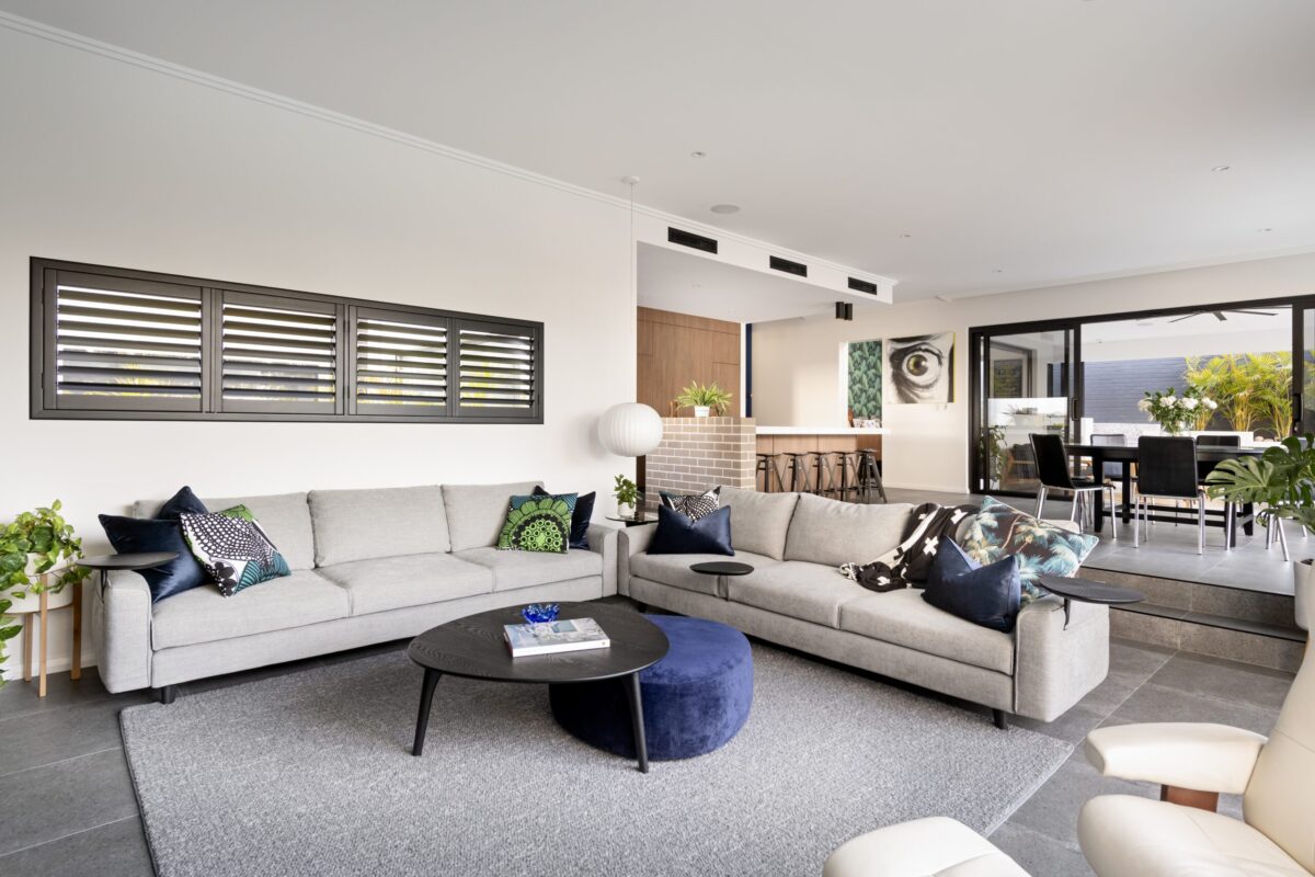 Open plan living with cream sectional lounge, plantation shutters and dining beyond