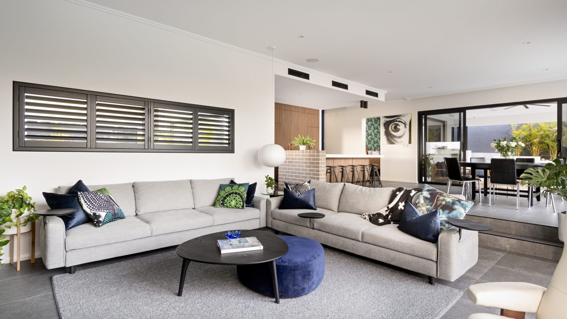 Open plan living with cream sectional lounge, plantation shutters and dining beyond
