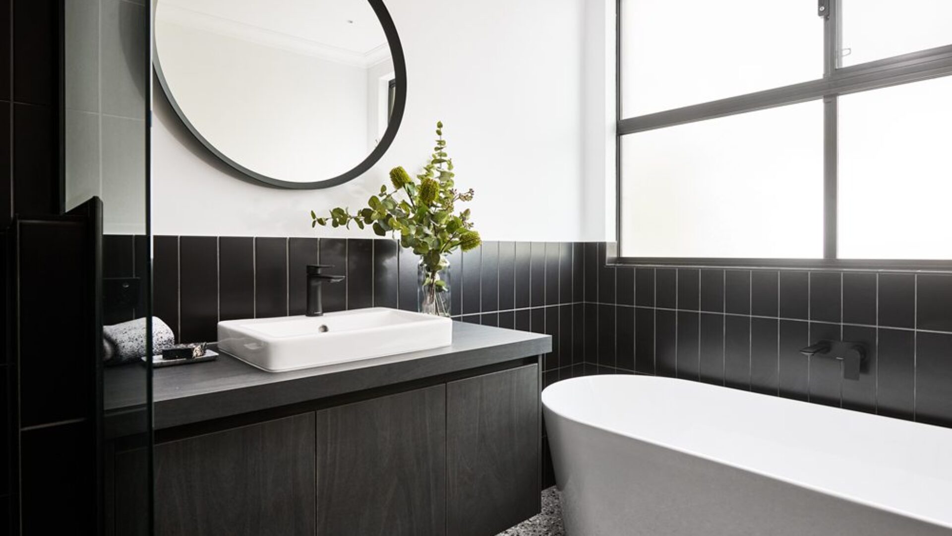 Bathroom with black tiling, round mirror and freestanding bath