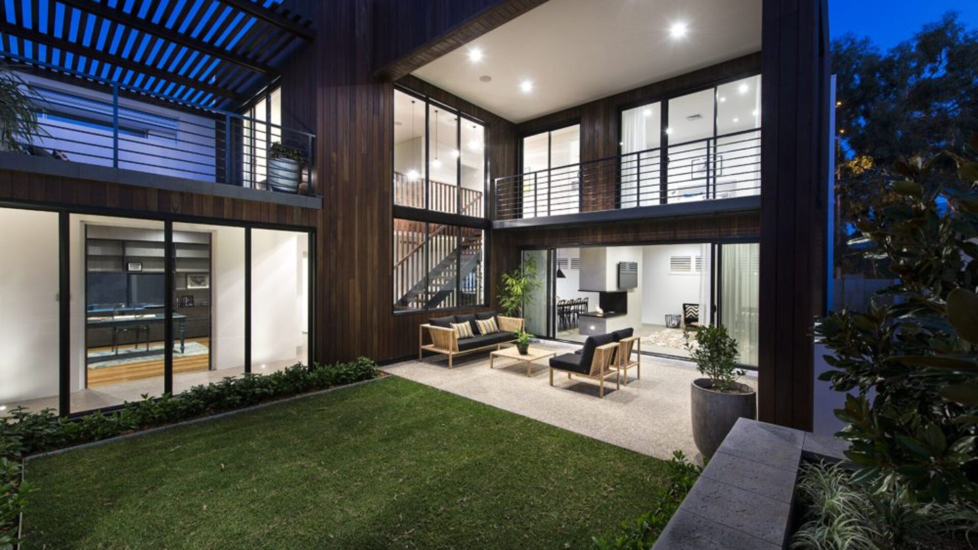 Two storey home courtyard at night with lawn and covered outdoor area