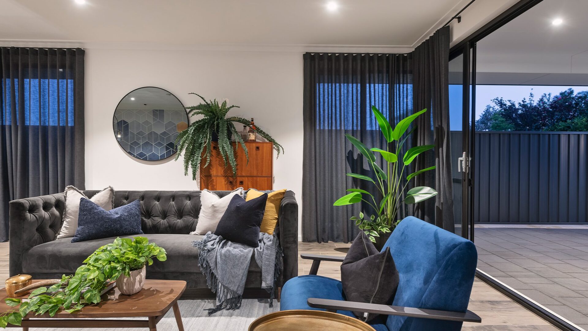 Living room at night with buttoned sofa, blue armchair and indoor plants