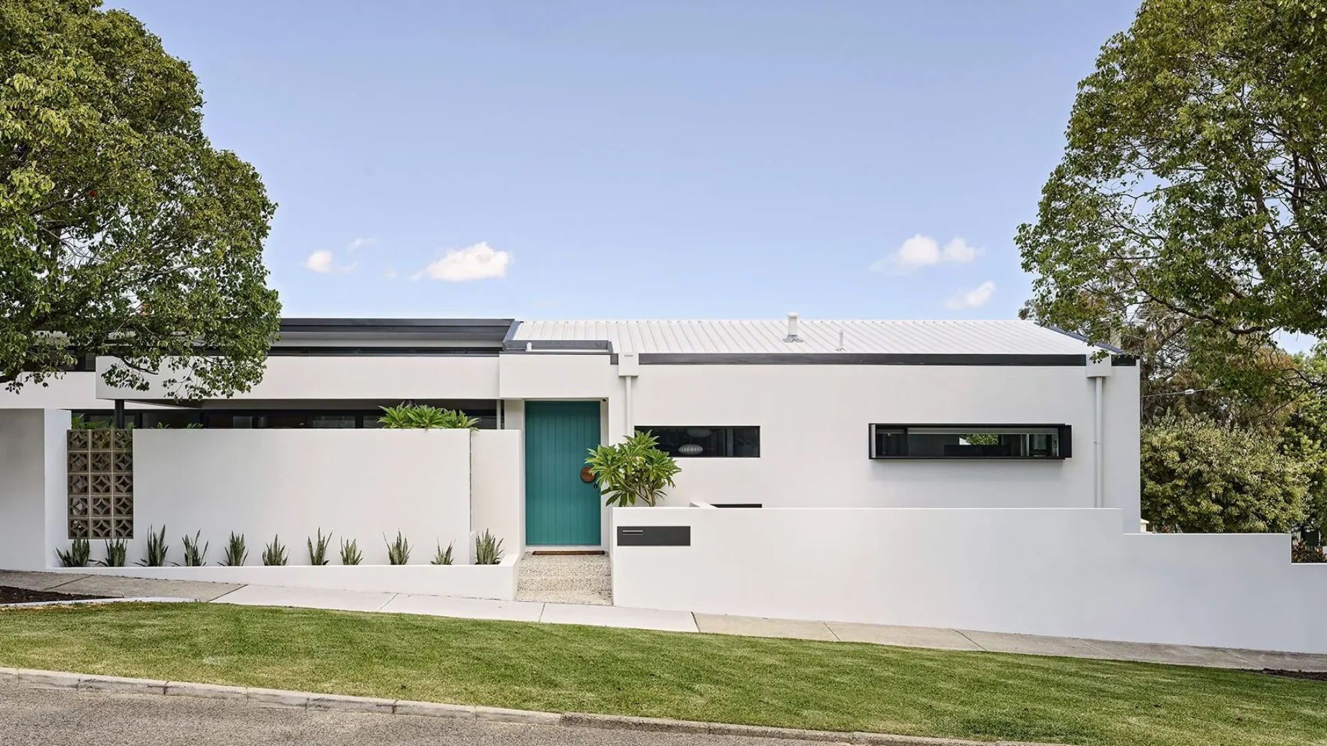 Single storey home facade with white render and teal front door