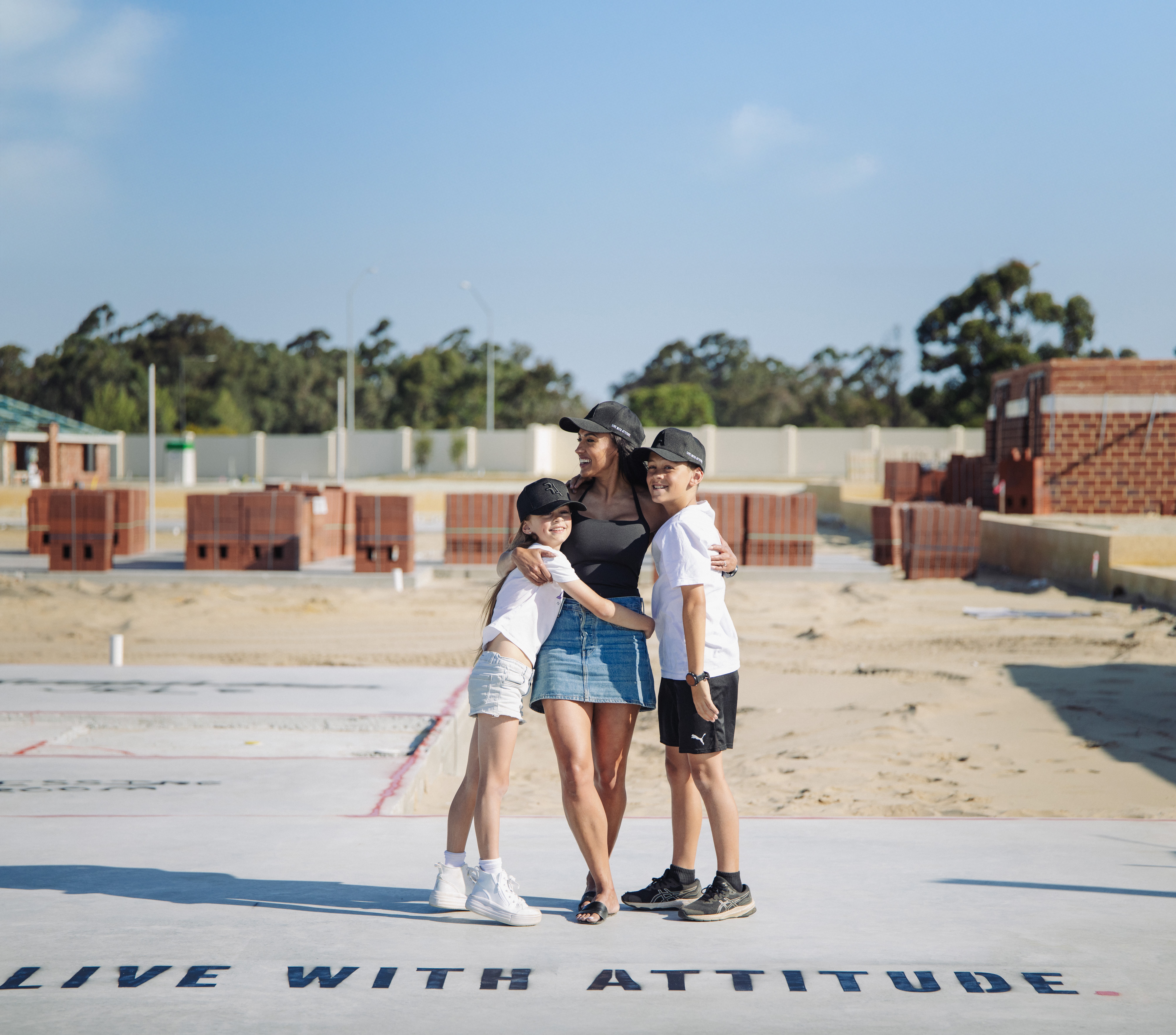 Family standing on a new home slab painted with Live With Attitude at a Perth building site