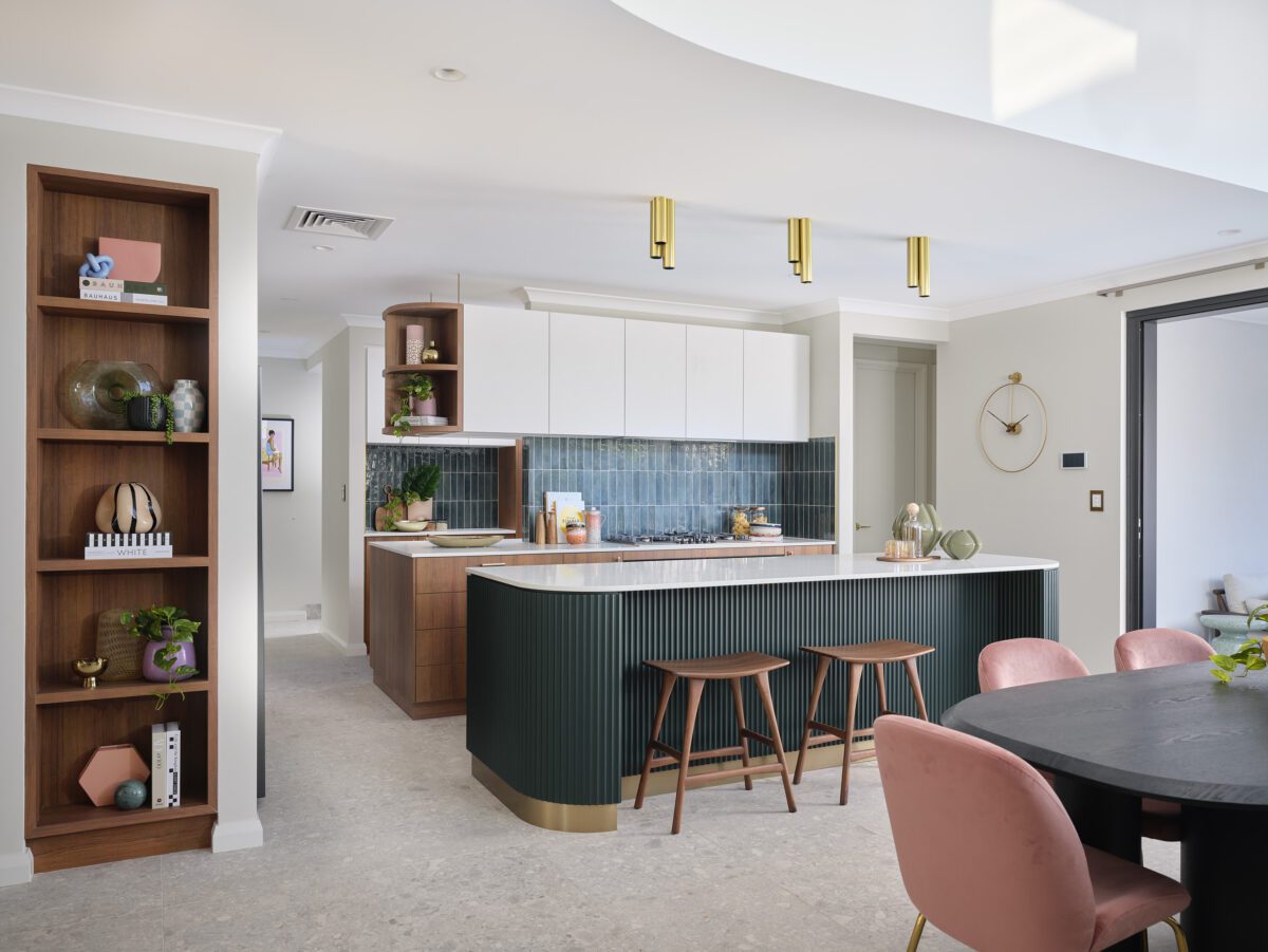 The Rubik’s Studio display features dark, forest green tiles, statement scalloped cladding panels, open shelves and island bench with seating in this mid-century modern meets contemporary home in Balcatta by Residential Attitudes. Interior selections by Jodie Cooper Design