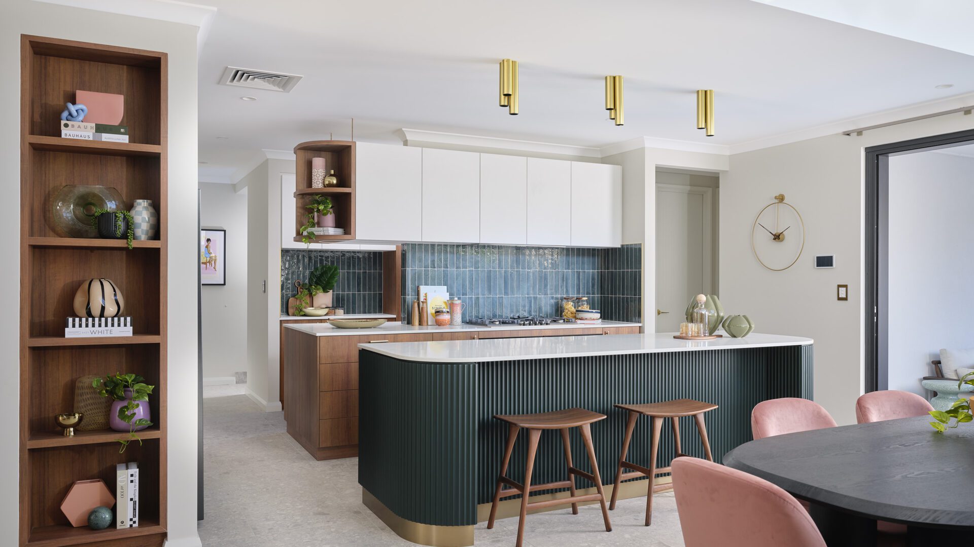 The Rubik’s Studio display features dark, forest green tiles, statement scalloped cladding panels, open shelves and island bench with seating in this mid-century modern meets contemporary home in Balcatta by Residential Attitudes. Interior selections by Jodie Cooper Design