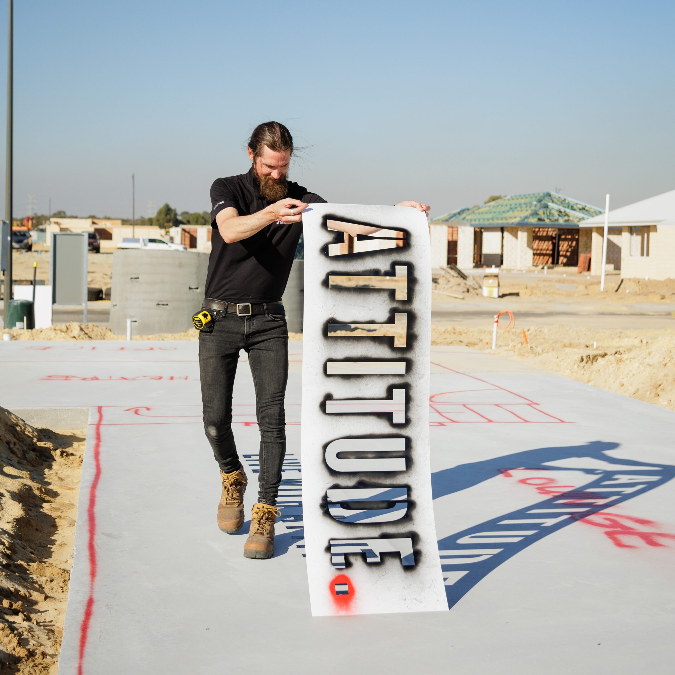 Team member holding an Attitude sign on a new home slab in a Perth estate