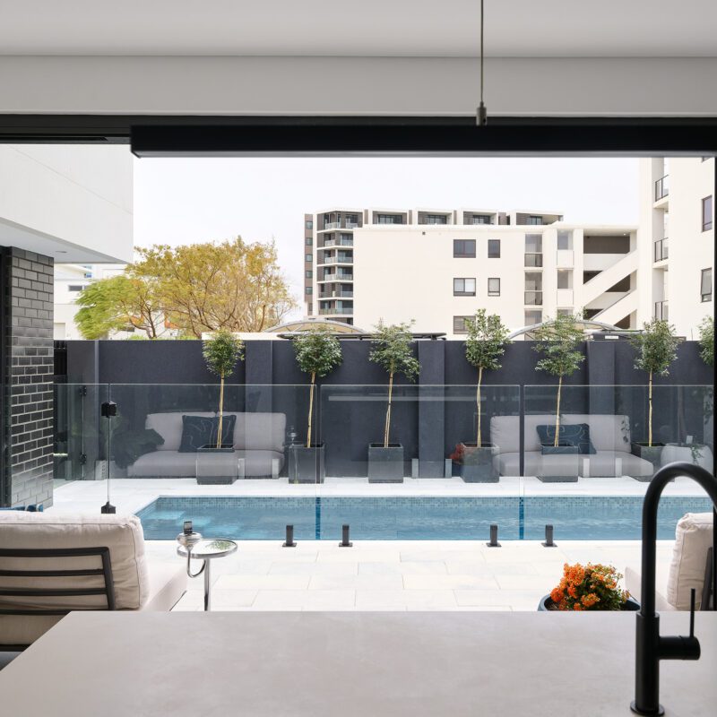 The photo shows the view from the kitchen island out toward an outdoor entertaining area with a glistening blue swimming pool for our North Coogee clients. Our clients share their experience and review Residential Attitudes.