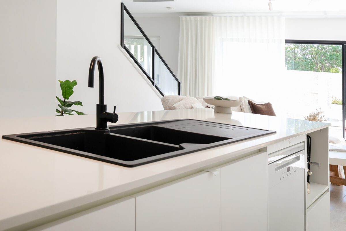 A contemporary black sink and black tapware accent the kitchen to make it pop! The double sink is placed on the island looking out toward the dining and living area. Built by Residential Attitudes.