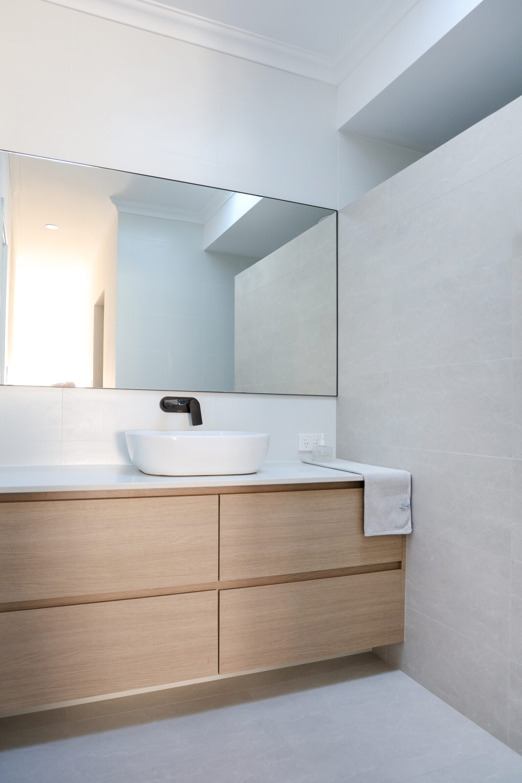 Black tapware at the basin in the bathroom, with a light grey tiled wall dividing the shower and vanity. Built by Residential Attitudes.