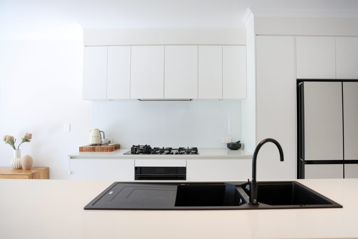 A contemporary white kitchen backdrop with black tapware and a black sink for our clients