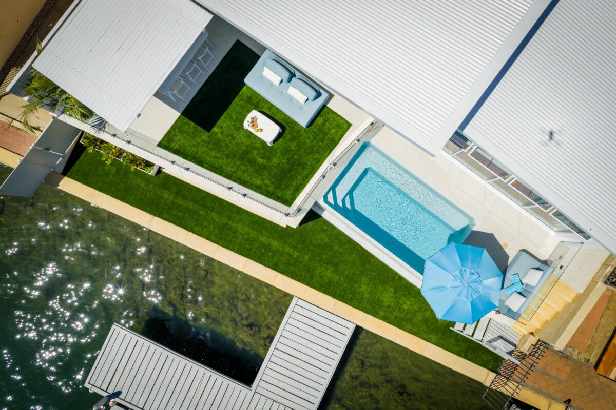 Aerial view of a client home built in Halls Head, Western Australia, on the canals. The view shows a lush green backyard, and a pool overlooking the canal from the backyard space. Built by Residential Attitudes.