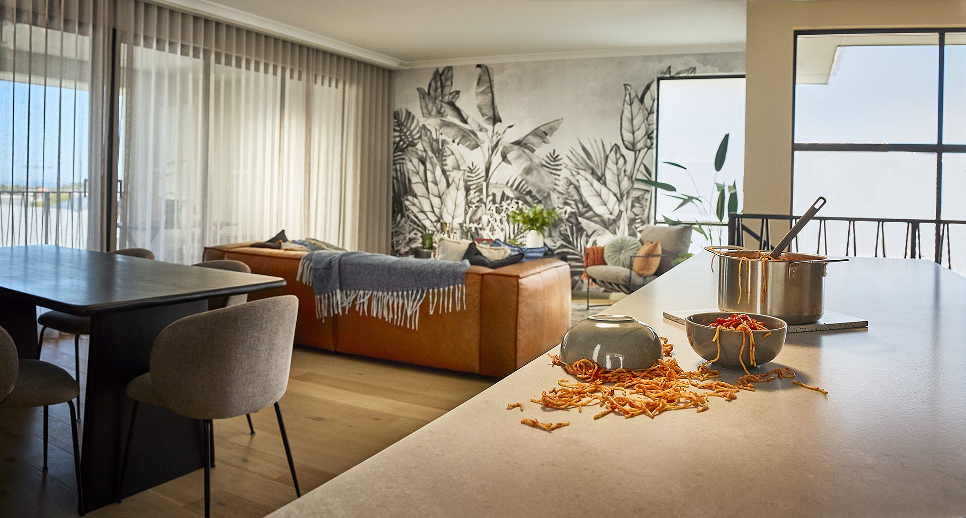 Perfect homes for imperfect lives in a Residential Attitudes home. There is spaghetti tipped over and in a mess on the stone-like benchtop of the Double Vision home. In the background, there is a jungle theme wallpaper that brings a sense of calm to the reverse-living space.